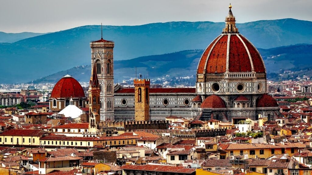 Best cities to visit in Europe: Panoramic view of Florence, Italy, dominated by the iconic red dome of the Florence Cathedral and Giotto's Campanile, set against rolling hills.