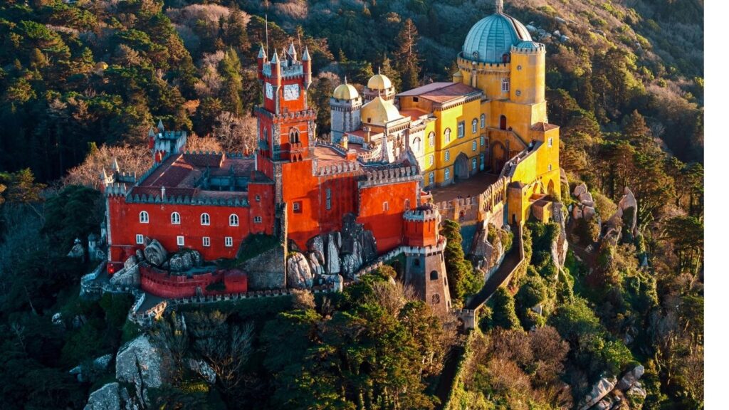 Best cities to visit in Europe: Aerial view of the colorful Pena Palace perched atop a hill in Sintra, Portugal, surrounded by lush green forests.